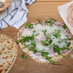 piadina romagnola z nałożoną mortadelą w plastrach orz świeżą rukolą i posypana startym parmezanem