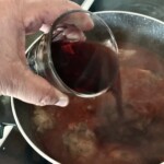 wlewanie szklanki czerwonego wina do gotującego się gulaszu