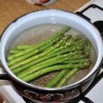w dużym garnku gotują się zielone szparagi
