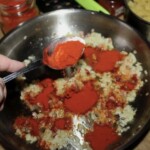 wsypanie mielonej słodkiej papryki do smażącej się na patelni cebuli