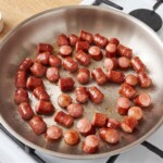 na dużej patelni smażą się pokrojone w małe kawałki frankfurterki