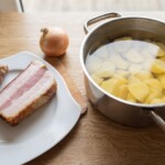 obrane i pokrojone ziemniaki znajdują się w garnku z wodą, obok plaster boczku