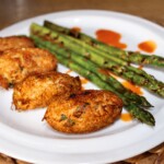 krokiety z dorsza suszonego podane na talerzu z grillowanymi zielonymi szparagami
