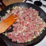 krojona w kostkę wieprzowina i siekana cebula smażą się na dużej patelni