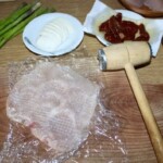 kotlet z kurczaka ubijany tłuczkiem na desce kuchennej