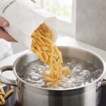 makaron penne wrzucany jest d garnka z gotująca się wodą