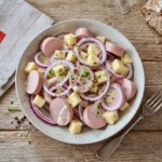 Sałatka szwajcarska z krojonego twardego sera Gruyere, cebuli i kiełbasy parówkowej polana sosem winegret z dodatkiem musztardy.