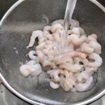 krewetki koktajlowe są płukane pod wodą na sitku