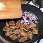 pokrojona w kostkę cielęcina smaży Sieną patelni razem z drobno siekaną czerwoną cebulą