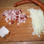 na blacie kuchennym leży łask kiełbasy oraz pokrojony w drobną kostkę boczek