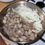 na patelni smaży się wieprzowina pokrojona w niedużą kostkę razem z cebulą pokrojoną w piórka