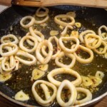 na patelni smażą się krążki kalmarów z siekanym czosnkiem na oliwie
