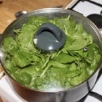 w dużym garnku pod pokrywką gotują się liście szpinaku