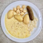 raclette z ziemniakami gotowanymi i kiszonkami podany na talerzu