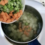 w garnku gotują się mrożony groszek i marchewka