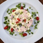 Sałatka z ziemniaczana z jajkami, kiełbasą parówkową i ogórkiem kiszonym połączonymi majonezem.