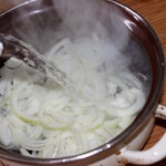 posiekana w piórka cebula zalewana jest wrzącą wodą w garnku