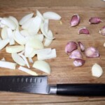 posiekana w piórka cebula oraz ząbki czosnku leżą na desce kuchennej