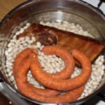 w dużym garnku leży żeberko wędzone, kiełbaski oraz bała fasolka suszona