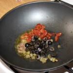 na patelni wok smażą się drobno pokrojone oliwki, suszone pomidory i kapary