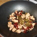 na patelni wok smażą się drobno pokrojone oliwki, suszone pomidory, kapary i kawałki łososia