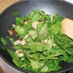 na patelni wok smażą się drobno pokrojone oliwki, suszone pomidory i kapary i liście szpinaku