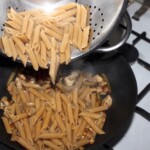 makaron penne ugotowany wrzucany jest do woka z przesmażonym mięsem z indyka cukinią oraz papryką