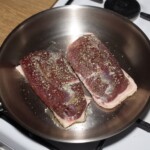 piersi z kaczki smażą się na dużej patelni skóra do dołu