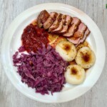 pierś z kaczki z żurawiną w sosie własnym podana z modrą kapustą i kluskami śląskimi na talerzu