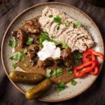 gulasz w sosie grzybowym podany na talerzu z kasza jęczmienną oraz ogórkami kiszonymi