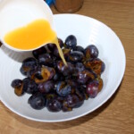 wypestkowane śliwki w misce zalewane są sokiem pomarańczowym