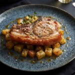 Kotlet schabowy marynowany w oliwie, musztardzie, czosnku i oregano, a następnie pieczony razem z ziemniakami.