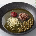 na patelni w sporej ilości oliwy smażą się fileciki anchois, kapary oraz siekana cebula i koncentrat pomidorowy