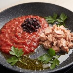 na patelni w sporej ilości oliwy smażą się fileciki anchois, kapary oraz siekana cebula i koncentrat pomidorowy i przecier pomidorowy