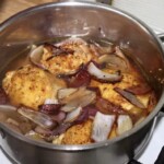 w garnku duszą się udka z kurczaka oraz kawałki czerwonej cebuli