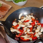 w woku smażą się małe kawałki piersi z kurczaka oraz paski czerwonej papryki