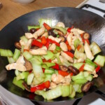 w woku smażą się małe kawałki piersi z kurczaka, paski czerwonej papryki i kawałki kapusty pekińskiej