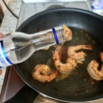 na patelni smażą się obrane krewetki i dolewane jest ouzo