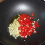 w woku smażą się drobno pokrojone cebula i czerwona papryka