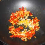 w woku smażą się drobno pokrojone cebula i czerwona papryka