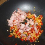 w woku smażą się drobno pokrojone cebula, czerwona papryka i siekana golonka