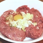 mięso mielone w misce razem z wbitym jajkiem i drobno siekaną cebulą