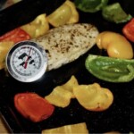 pokrojone w kostkę kolorowe papryki na blasze w trakcie pieczenia z piersią kurczaka