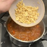 ugotowana zmiażdżona ciecierzyca wrzucana jest do garnka z zupą chilli