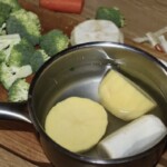 duży obrany i przekrojony na połowę ziemniak w garnku z wodą