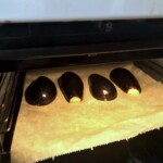 pokrojone wzdłuż na połowę dwa bakłażany leżą na blasze do pieczenia w piekarniku