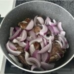 w garnku smażą się kawałki mięsa razem z pokrojoną czerwoną cebulą