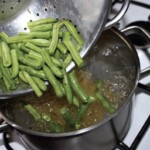 zielona fasolka szparagowa wrzucana jest z durszlaka do garnka z gotującą się wodą