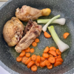 kawałki kurczaka smażą się na patelni z krojonymi warzywami