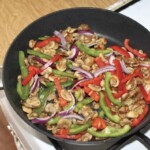 na patelni smażą się pokrojone w paski kolorów papryki, czerwona cebula i paski mięsa